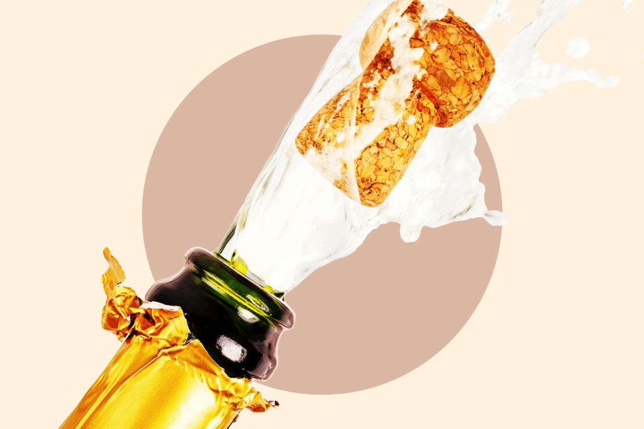 Close up of a champagne bottle popping on a tan background