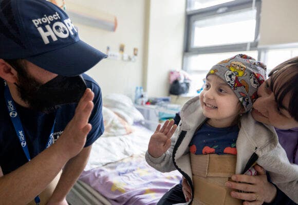 Project HOPE member waving to woman and smiling 5-year-old patient at University Children’s Hospital in Krakow.